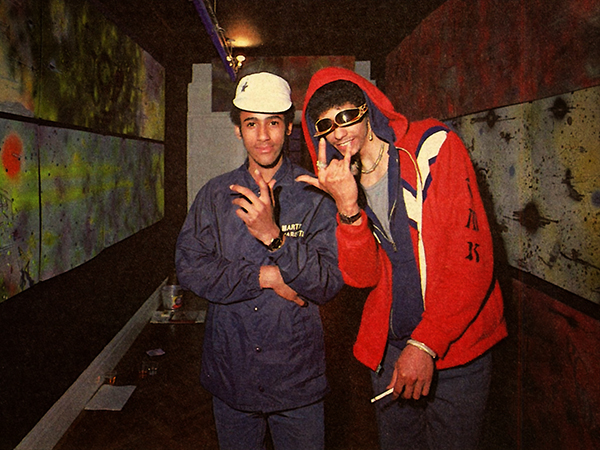K-Rob and Rammellzee in a hallway of paintings