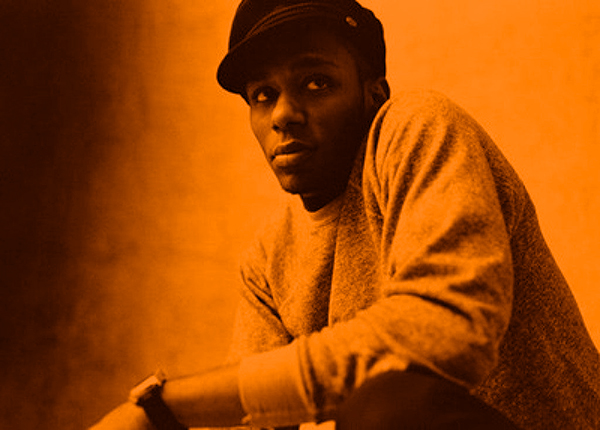 Classic promo shot of Mos Def crouching in a thoughtful stance.